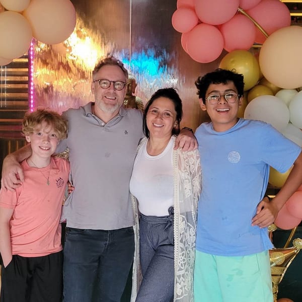 A family of four smiling in front of a decorative wall with balloons and a waterfall.