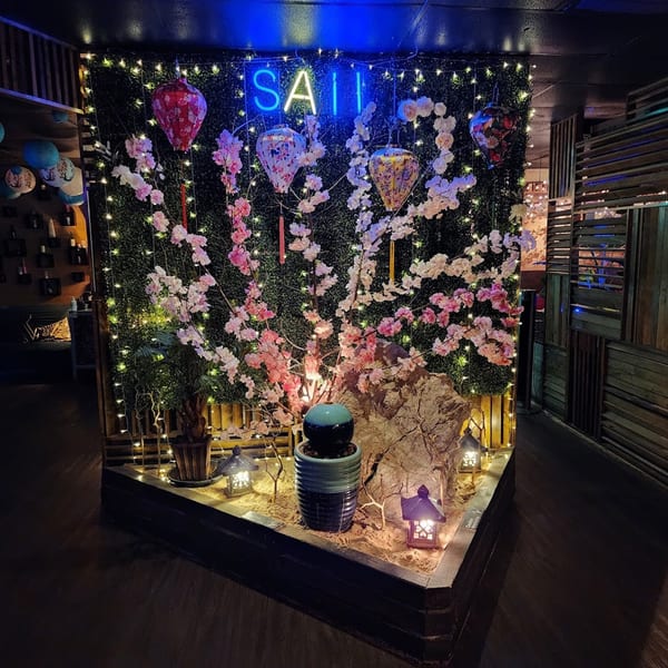 A Saii Asian Bistro and Sushi Bar interior with a neon sign, cherry blossoms, lanterns, and string lights.