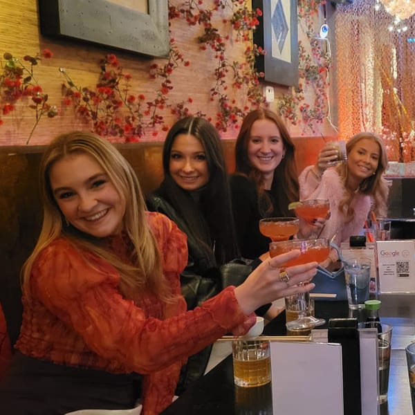 Four smiling women at Saii Asian Bistro and Sushi Bar, holding cocktails and enjoying the vibrant atmosphere.