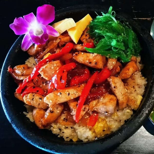 Saii Asian Bistro's chicken teriyaki bowl with rice, red peppers, seaweed salad, and a purple orchid.