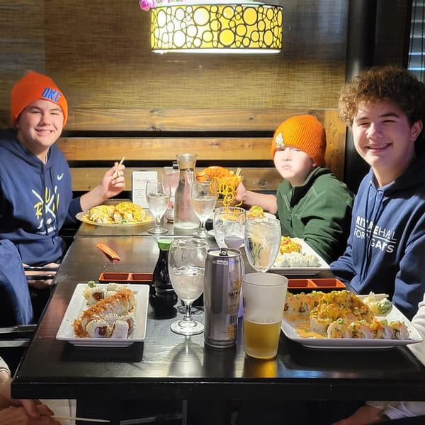 Three young men enjoying various sushi rolls and drinks at Saii Asian Bistro.