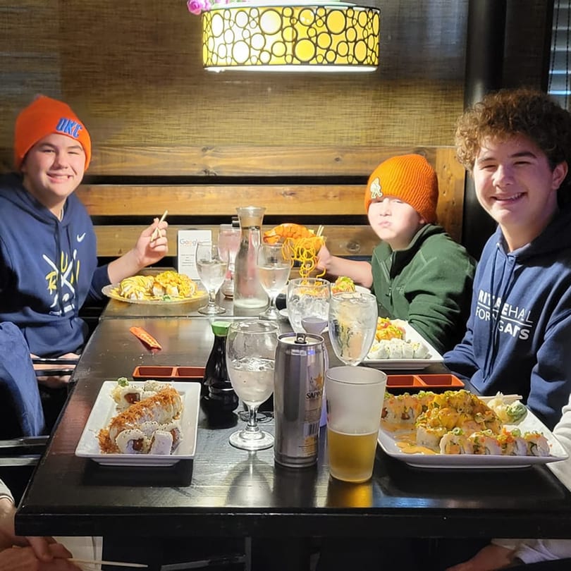 Three young men enjoying various sushi rolls and drinks at Saii Asian Bistro.