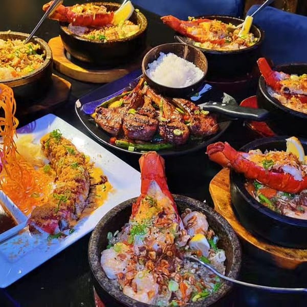 A table laden with various Saii Asian Bistro dishes, including sushi rolls, lobster tails, and grilled lamb chops.
