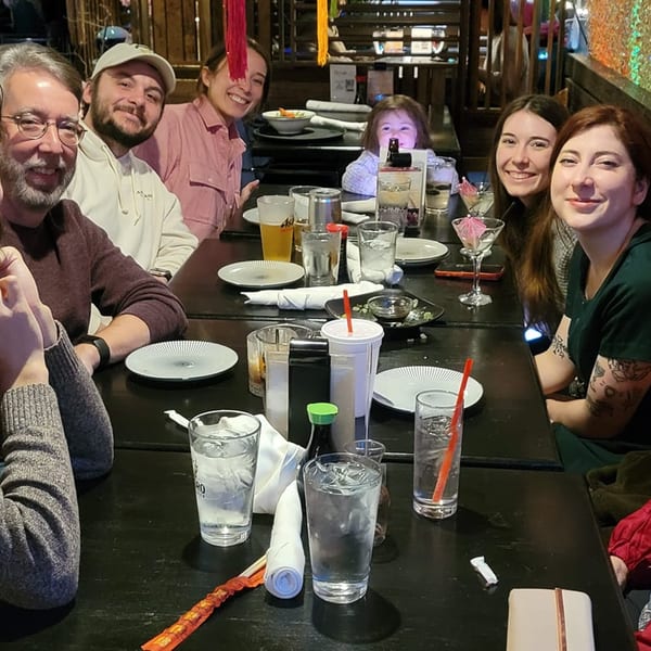 Group of people smiling at a table with drinks and plates at Saii Asian Bistro.
