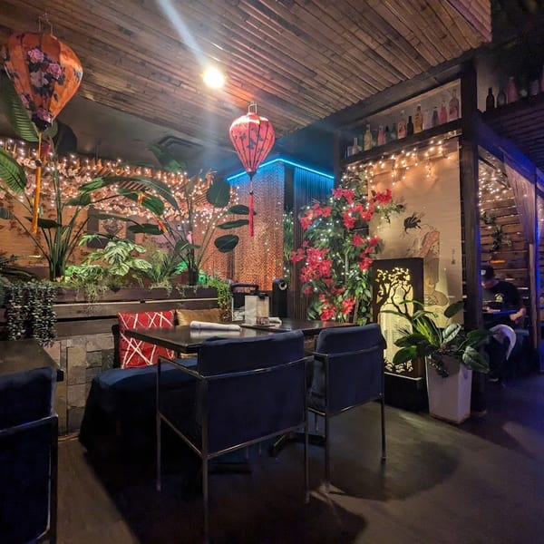 A dimly lit Saii Asian Bistro dining area with hanging lanterns, plants, and string lights.