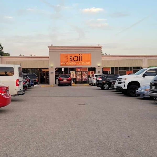Exterior of Saii Asian Bistro and Sushi Bar with an orange sign and cars parked in front.