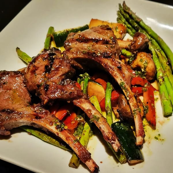 Grilled lamb chops with asparagus, zucchini, bell peppers, and mushrooms on a white plate.